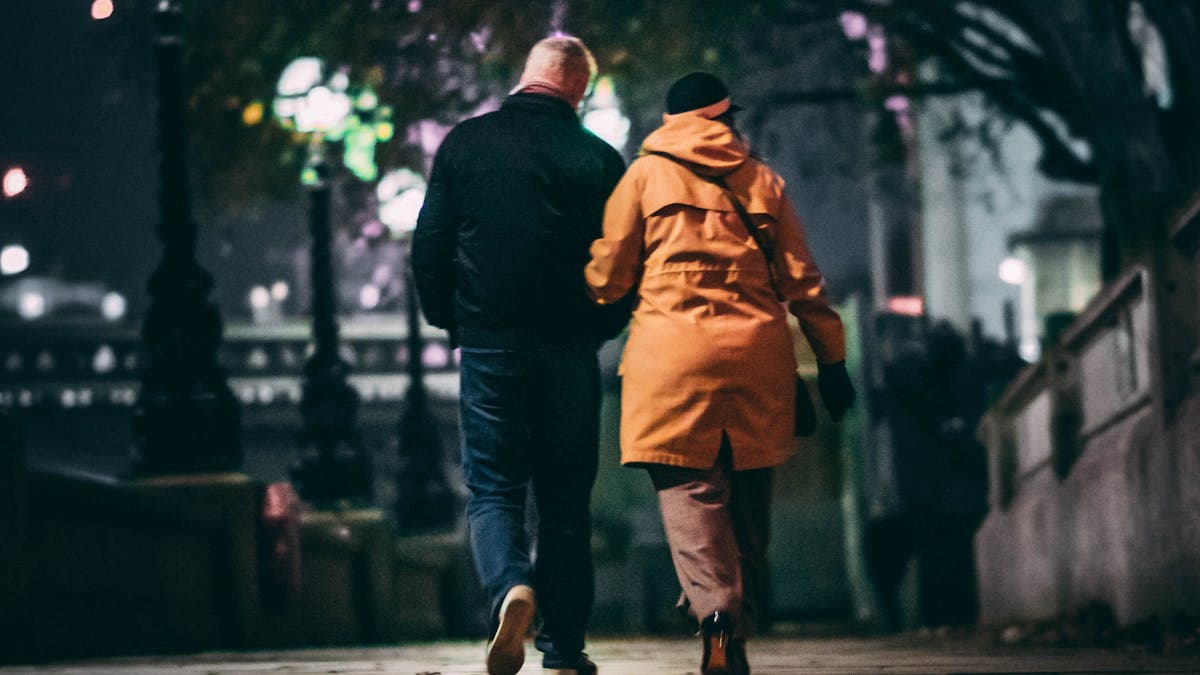 Couple walking hand in hand on a city sidewalk at night, illuminated by street lights
