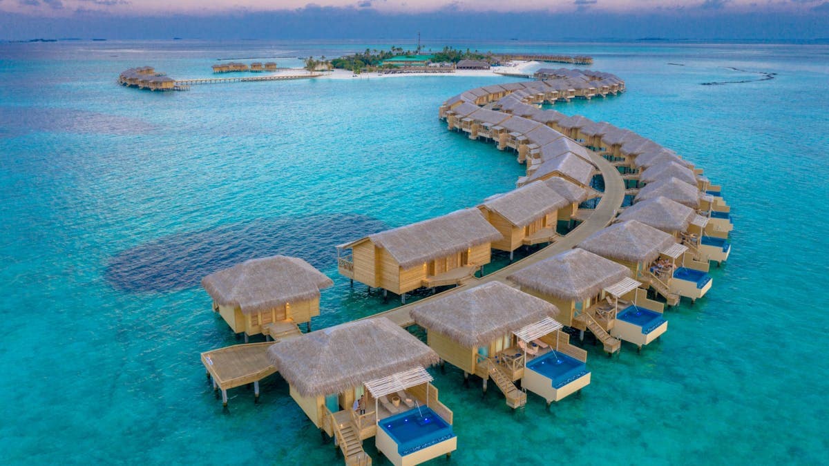 Luxury overwater water villas in the Maldives at sunset, with turquoise lagoon and tropical island backdrop