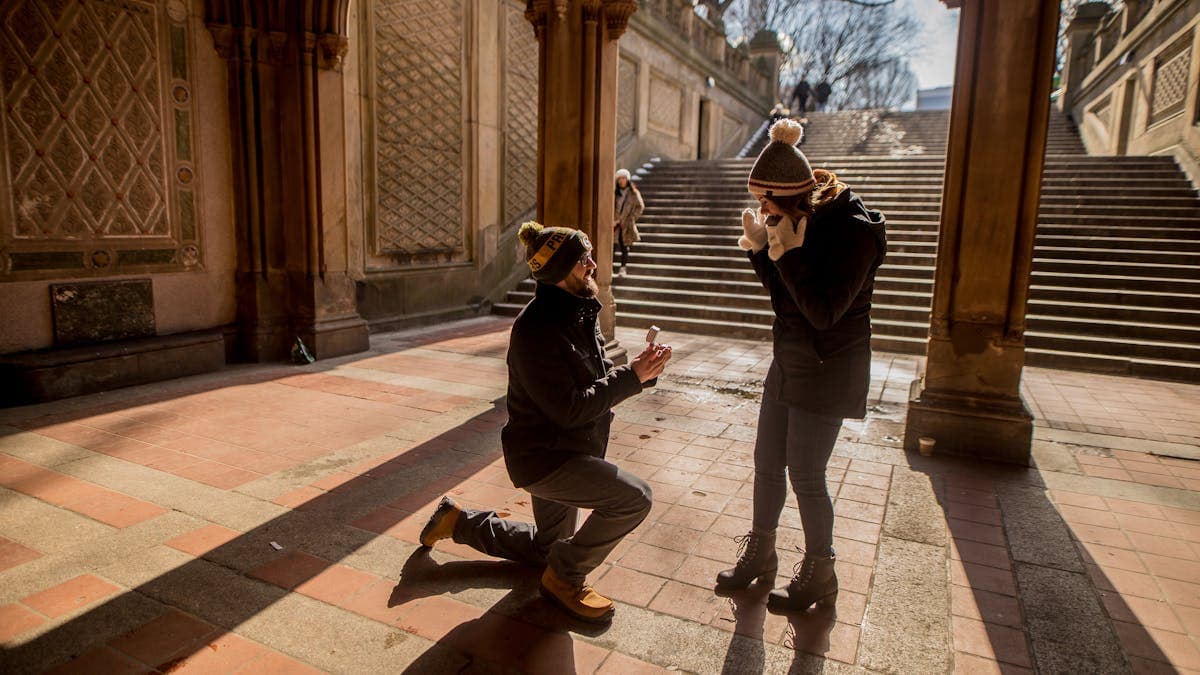 Man on one knee proposing to a woman in a romantic outdoor setting